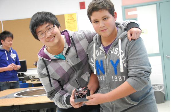 Two students hold piece of computer technology in classroom
